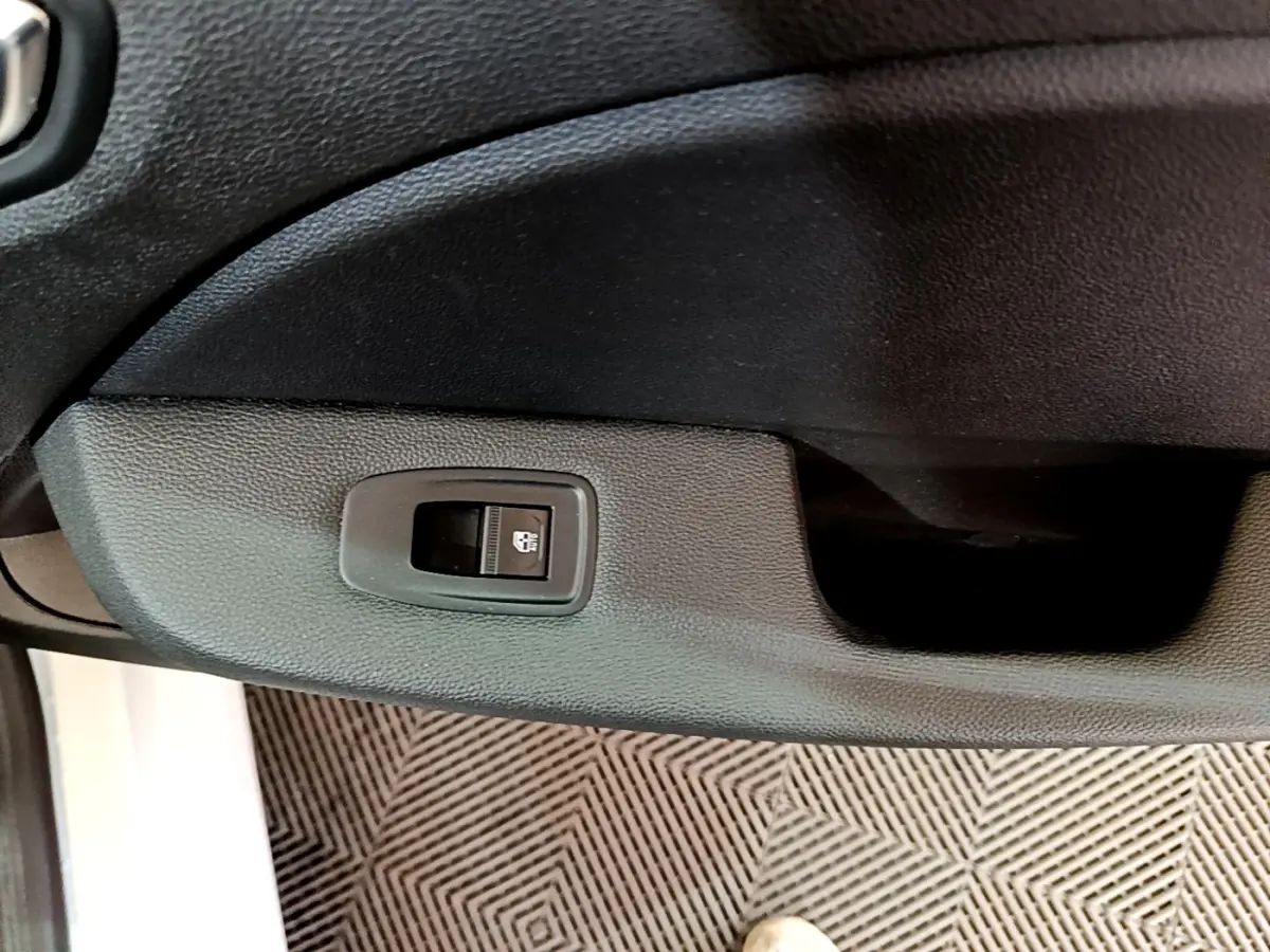 Bouton de commande de vitre sur la porte intérieure côté conducteur d'une Renault Clio blanche, vue rapprochée.