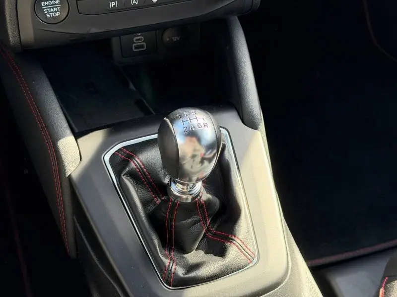 Le levier de vitesses manuel de la Ford Focus SW 2023 avec coutures rouges sur soufflet en cuir noir, vue rapprochée intérieure.