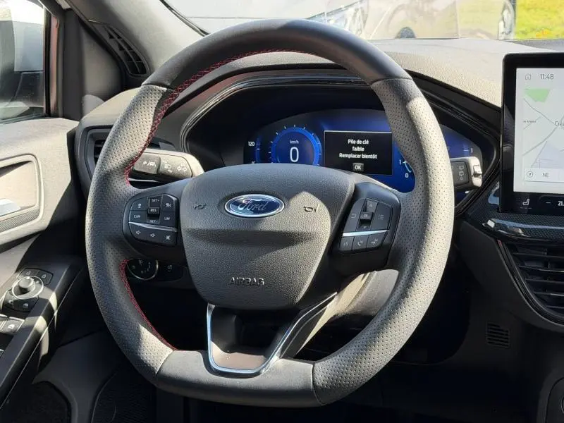 Vue intérieure centrée sur le volant perforé avec surpiqûres rouges du Ford Focus SW 2023, tableau de bord digital visible.