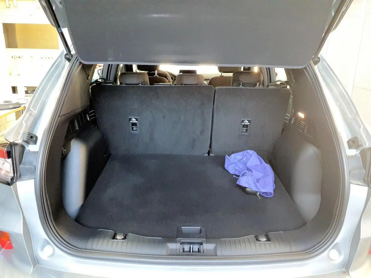 Coffre ouvert vu de l'arrière d'un Ford Kuga gris Solar 2024, avec intérieur noir et un tissu violet posé.