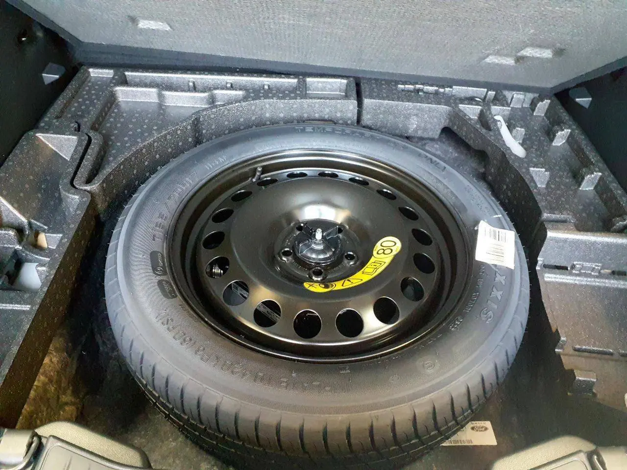 Roue de secours galette noire dans le coffre du Ford Kuga 2024, vue plongeante sur le pneu et son logement en mousse.