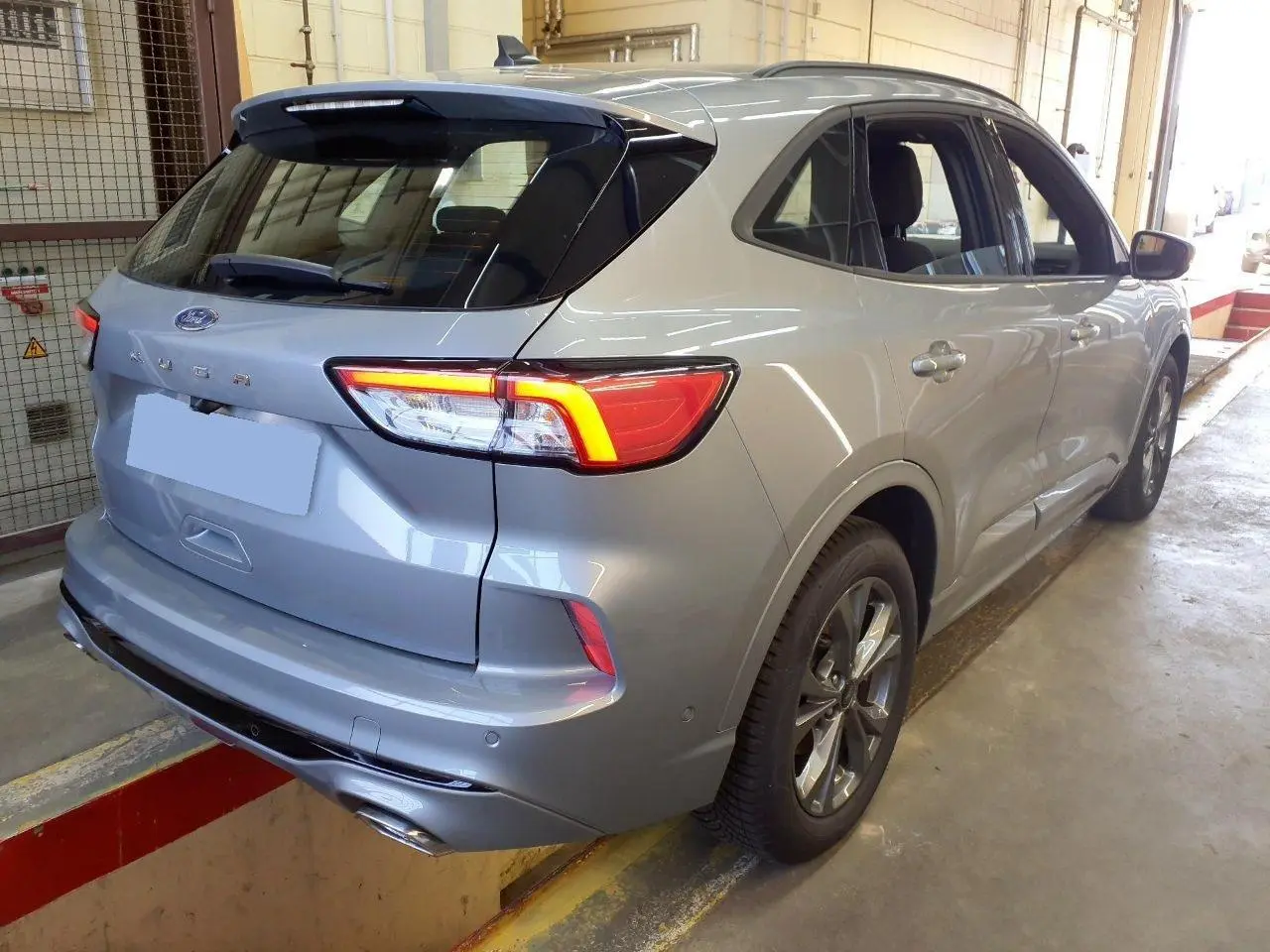 Vue 3/4 arrière droite du Ford Kuga gris Solar 2024 avec feux allumés et double sortie d’échappement ST-Line.