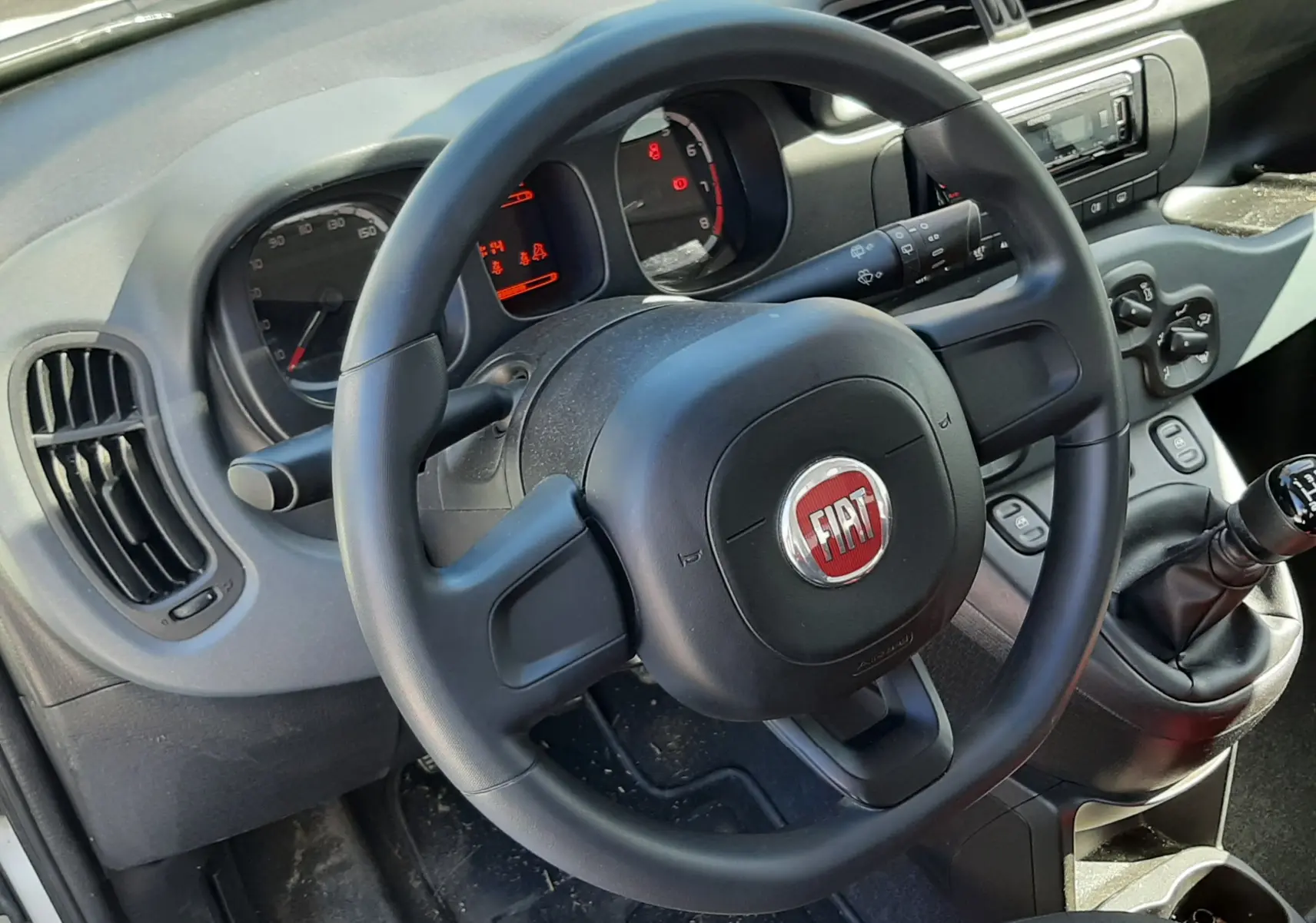 Vue intérieure centrée sur le volant noir FIAT et le tableau de bord de la Fiat Panda blanche de 2018 avec levier de vitesse manuel.
