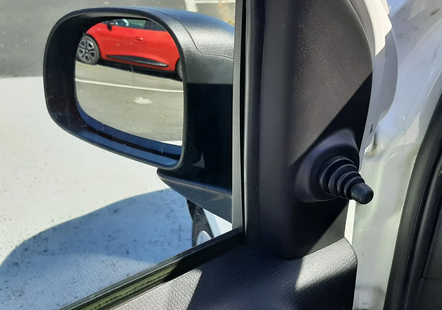 Rétroviseur côté gauche d'une Fiat Panda blanche 2018, avec vue sur une voiture rouge en arrière-plan.