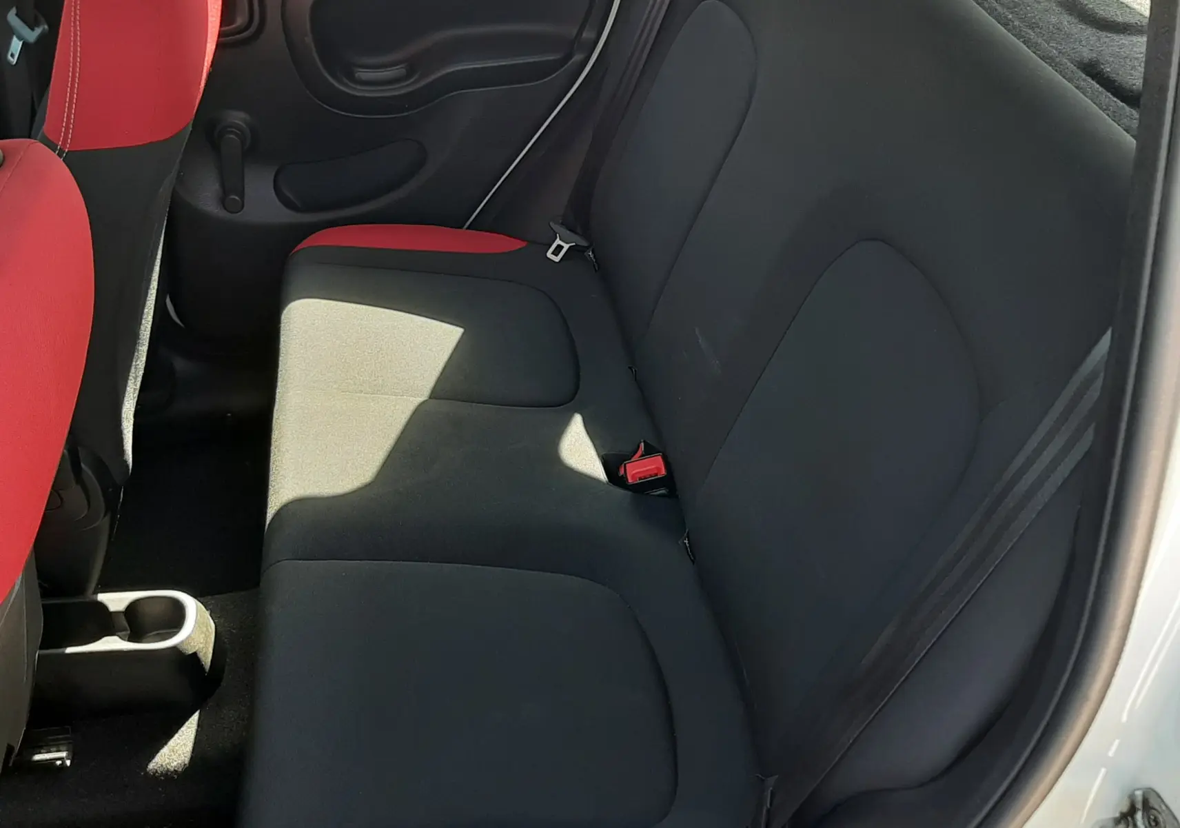 Vue intérieure arrière droite de la Fiat Panda 2018 avec sièges en tissu noir et rouge, portes blanches ouvertes.
