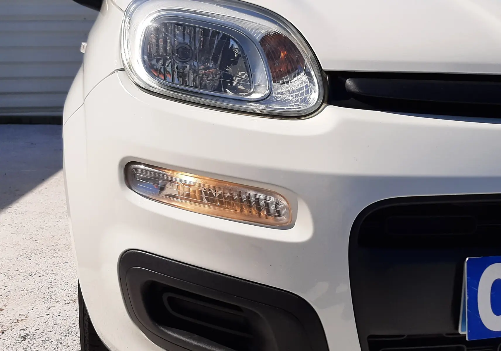 Gros plan sur l'avant gauche d'une Fiat Panda blanche 2018, mettant en valeur le phare et le clignotant.