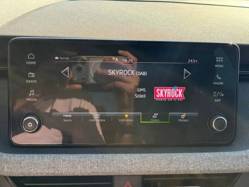 Écran tactile central de la Skoda Scala 2025 affichant la radio Skyrock avec commandes autour et finition tissu gris.