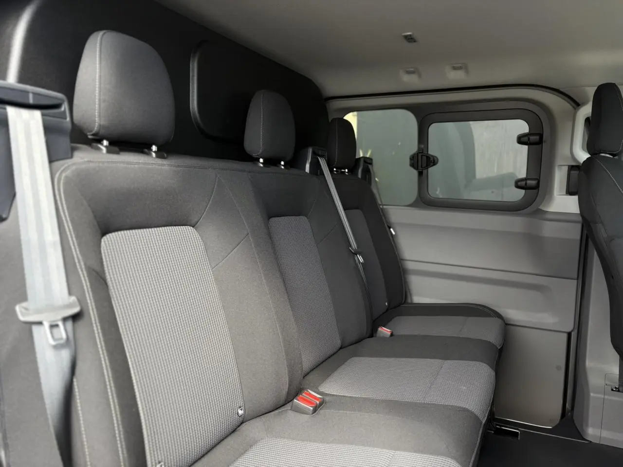 Vue intérieure côté droit des sièges arrière en tissu gris du Volkswagen Transporter T7 ProCab 2026, avec fenêtre coulissante.
