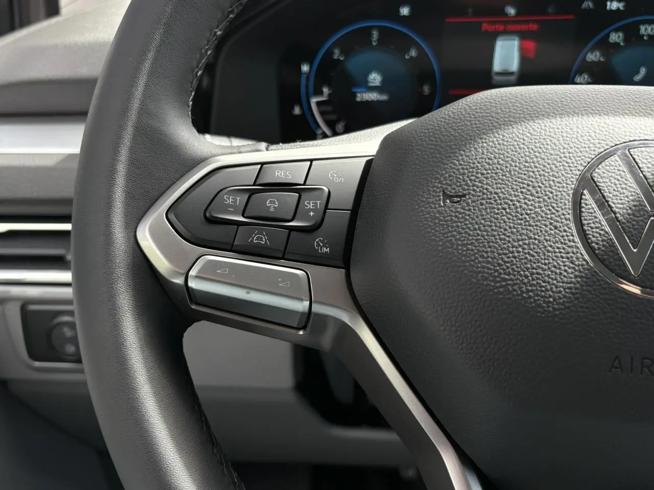 Gros plan sur le volant multifonction noir du Volkswagen Transporter T7 avec commandes de régulateur de vitesse et tableau de bord numérique en arrière-plan.