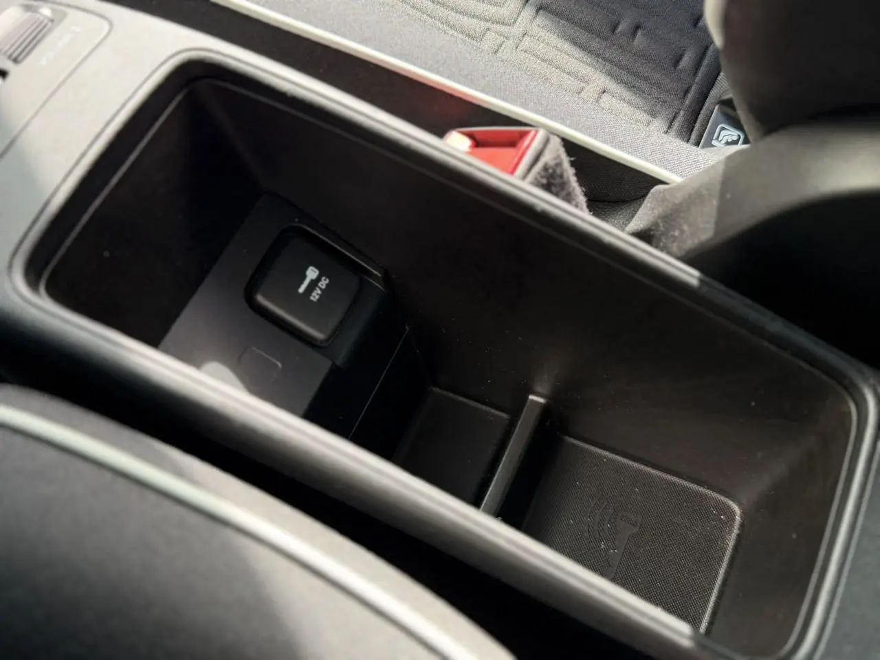 Gros plan sur le rangement central intérieur de la Fiat 500 électrique 2024, avec prise 12V visible et sellerie noire.