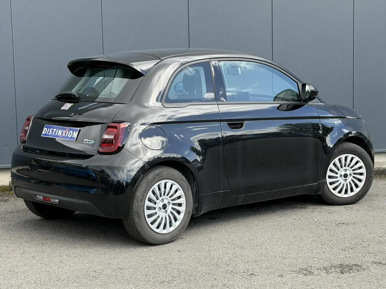 Vue 3/4 arrière droite d'une FIAT 500 électrique 2024 en noir Onyx avec jantes blanches et feux arrière LED.
