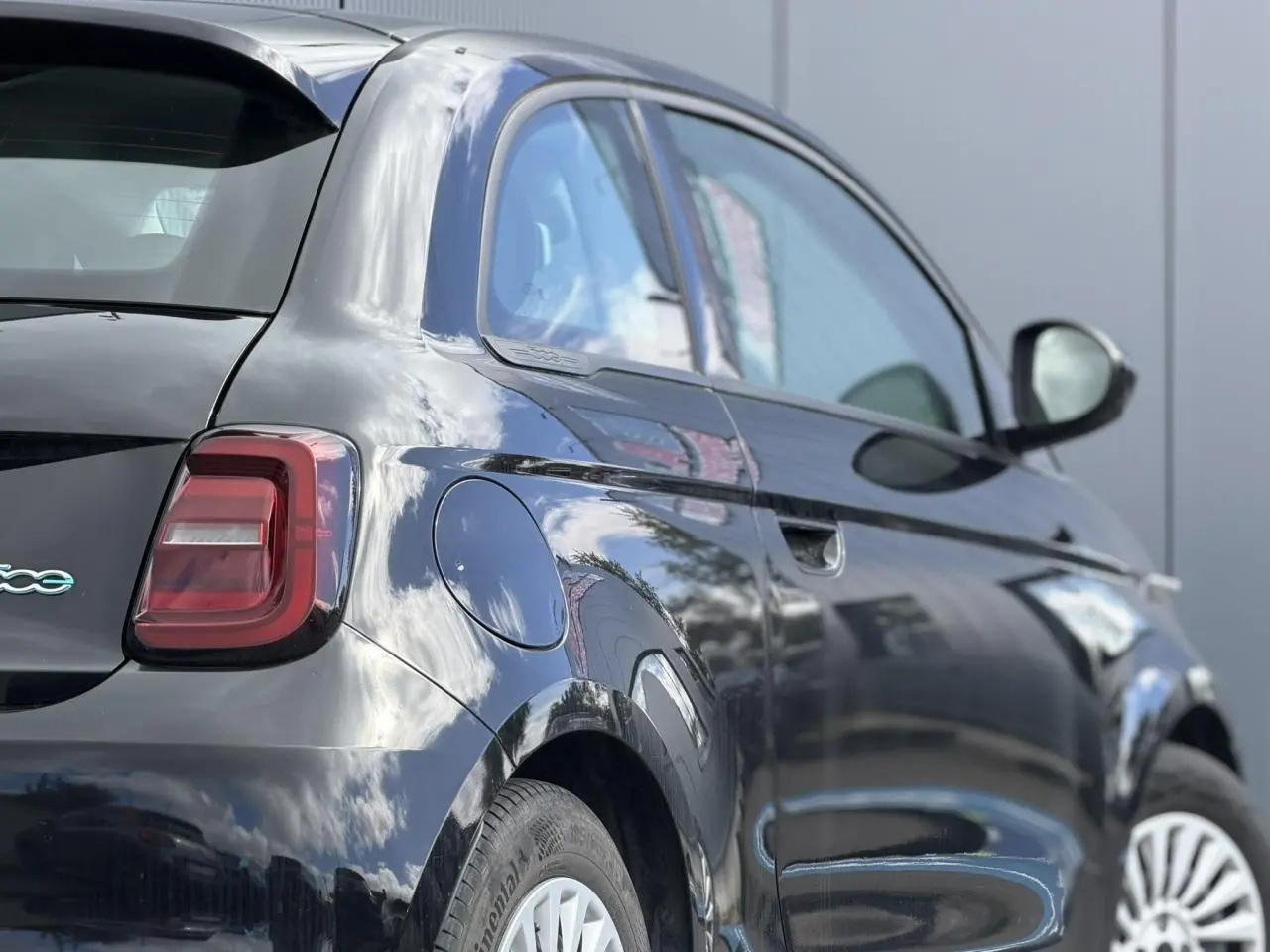 Vue 3/4 arrière droite de la Fiat 500 électrique 2024 en noir Onyx avec feux arrière LED et jantes blanches.