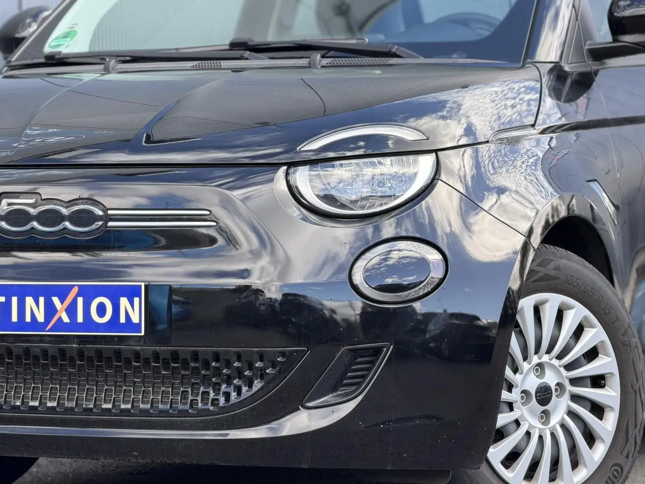 Gros plan 3/4 avant droit du Fiat 500 électrique 2024 en noir Onyx, mettant en valeur le phare rond et la calandre épurée.