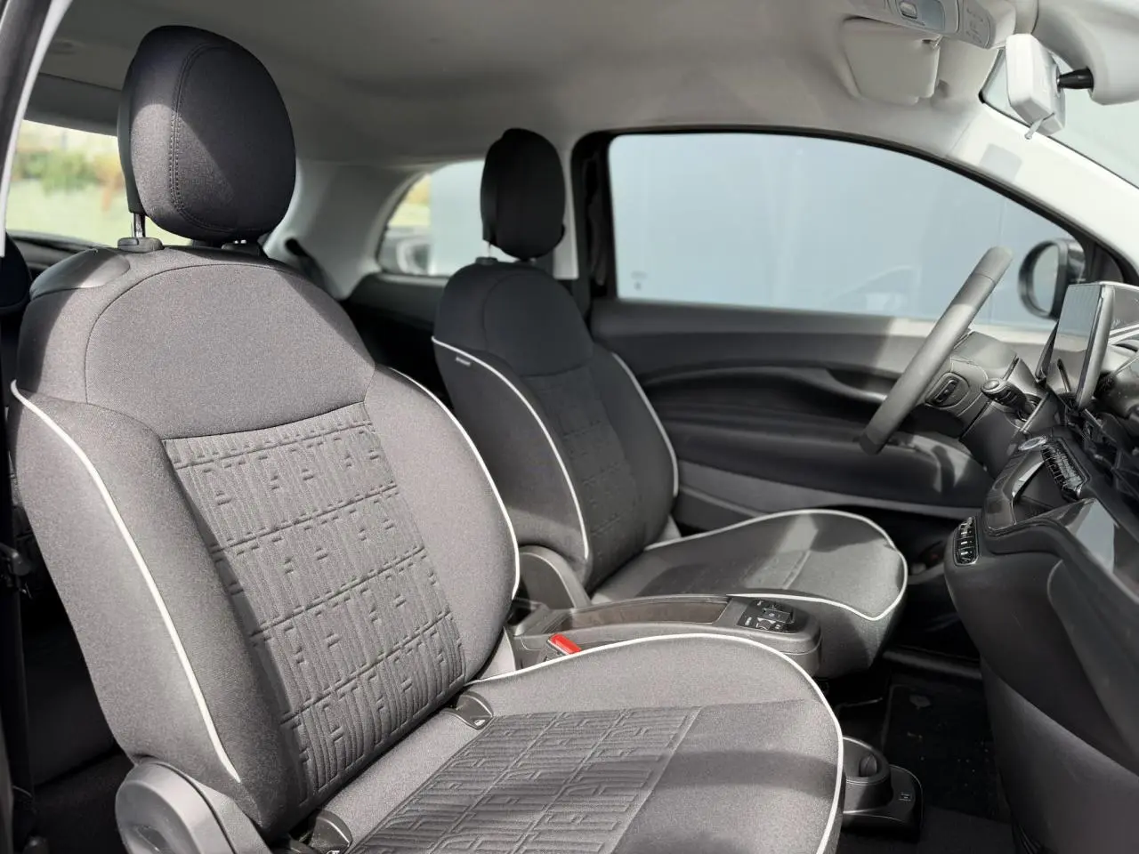 Vue intérieure côté droit montrant les sièges avant en tissu noir avec surpiqûres blanches d'une FIAT 500 électrique 2024.