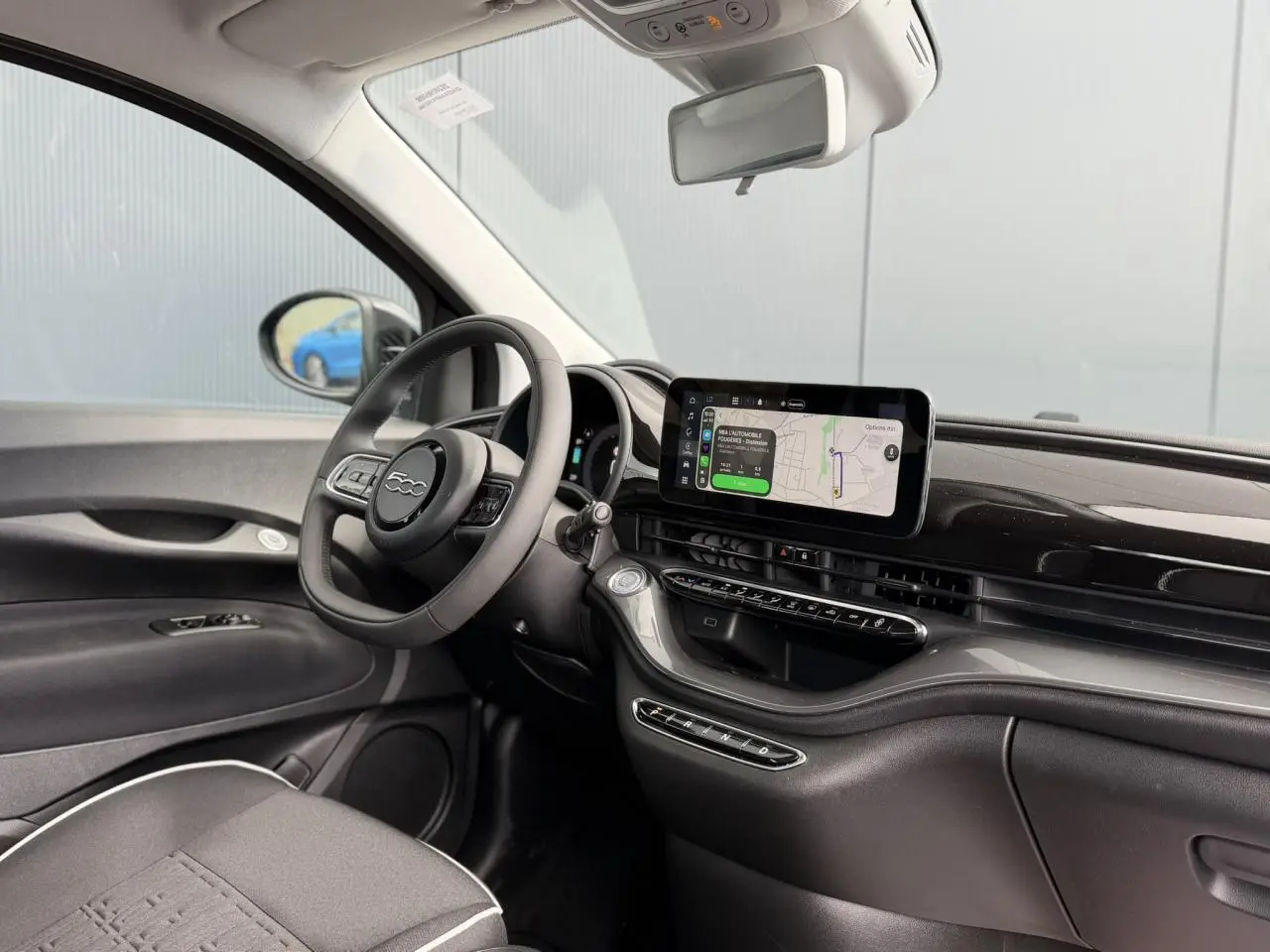 Intérieur de la Fiat 500 électrique 2024, vue côté conducteur, tableau de bord noir brillant avec écran tactile central.