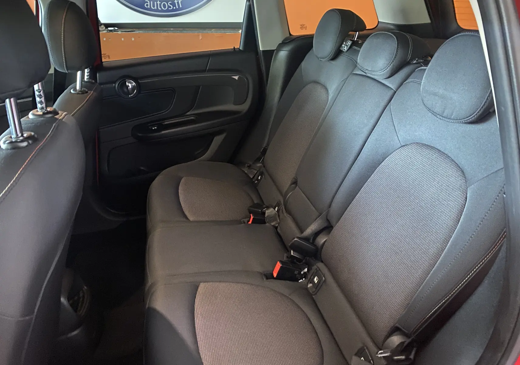 Vue intérieure montrant les sièges arrière en tissu noir d'une MINI Countryman rouge toit noir, avec appuie-têtes et ceintures visibles.