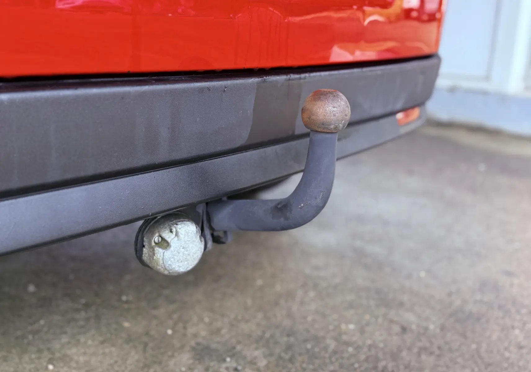 Gros plan sur l'attelage d'une FIAT Doblo Cargo rouge, avec pare-chocs arrière noir et prise électrique visible.