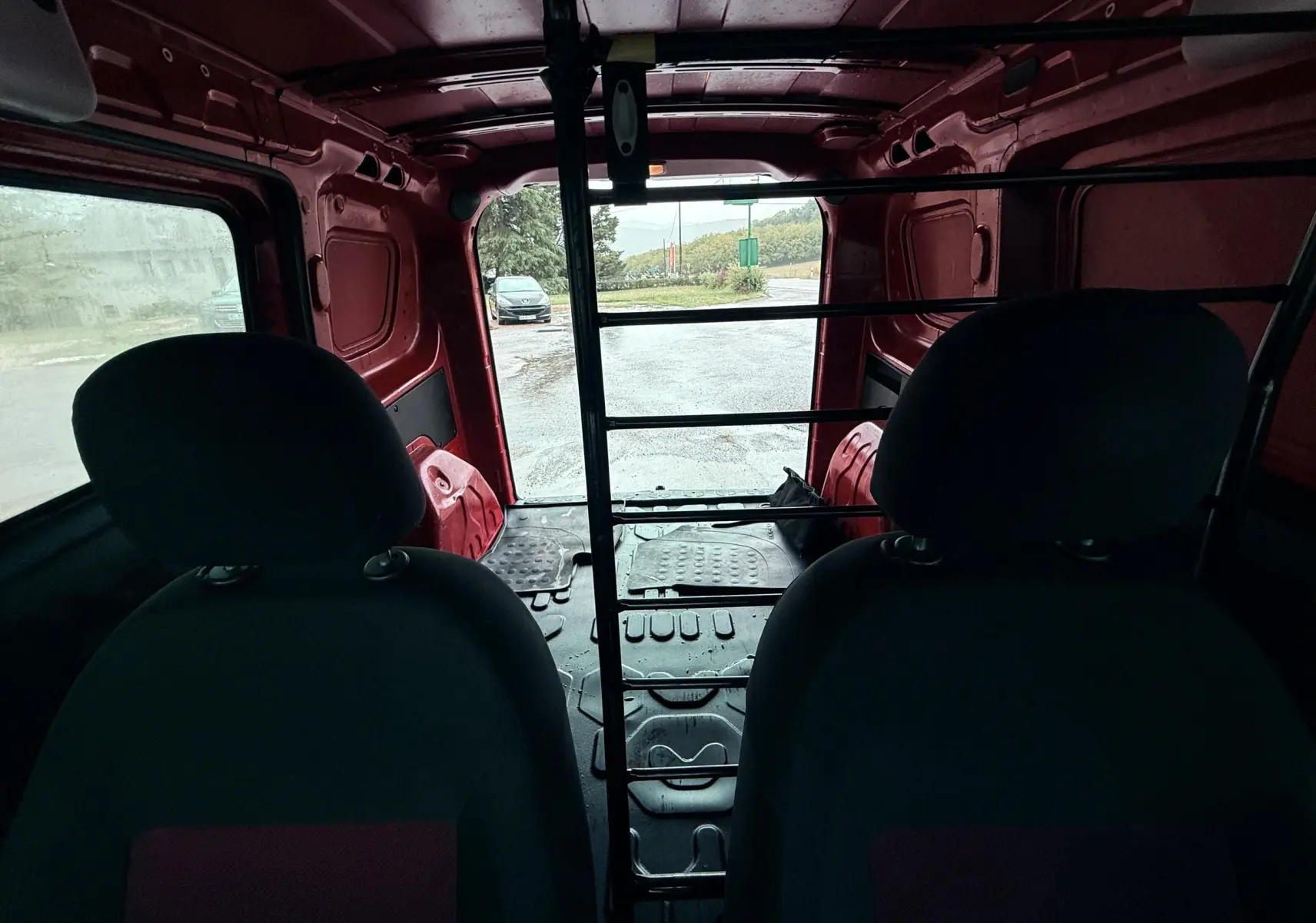 Vue intérieure arrière du Fiat Doblo Cargo rouge de 2011, montrant la cloison métallique et les sièges avant.