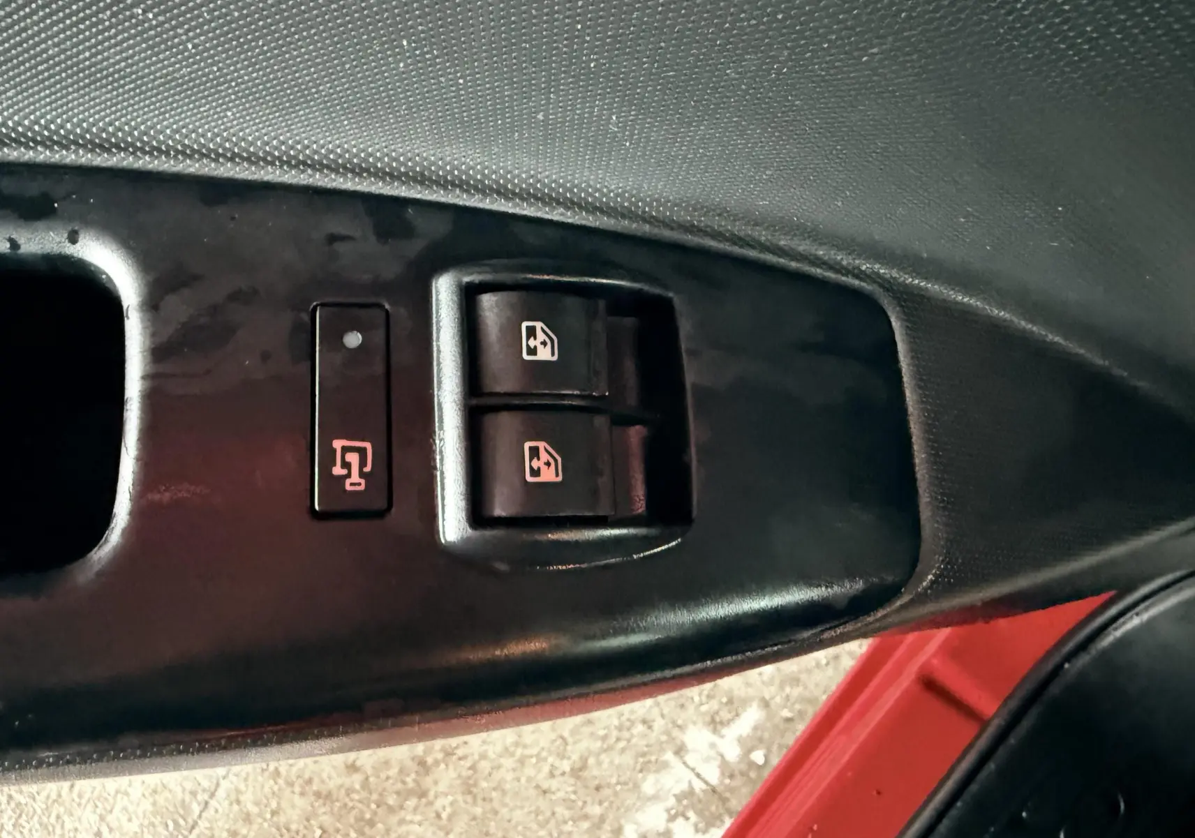 Gros plan sur les commandes de lève-vitres côté conducteur du FIAT Doblo Cargo rouge de 2011.