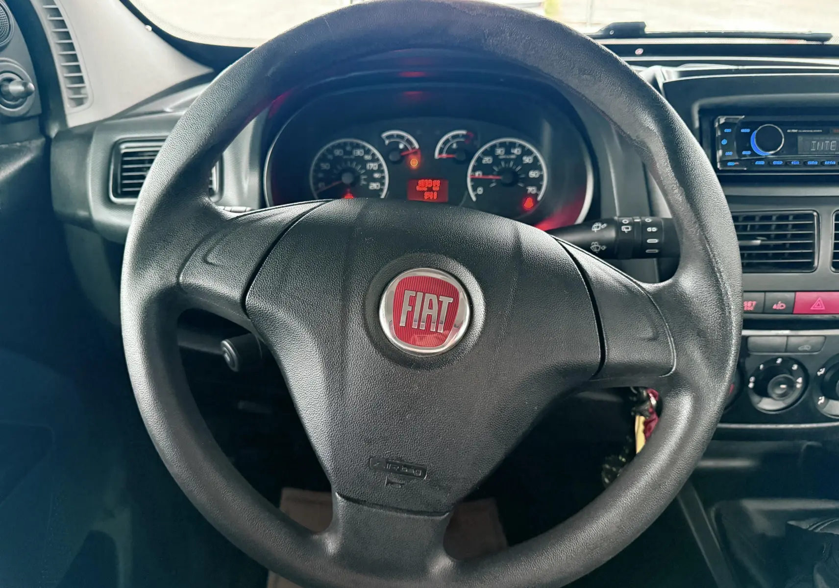 Vue rapprochée du volant noir avec logo FIAT rouge, tableau de bord et console centrale d’un Fiat Doblo Cargo 2011.