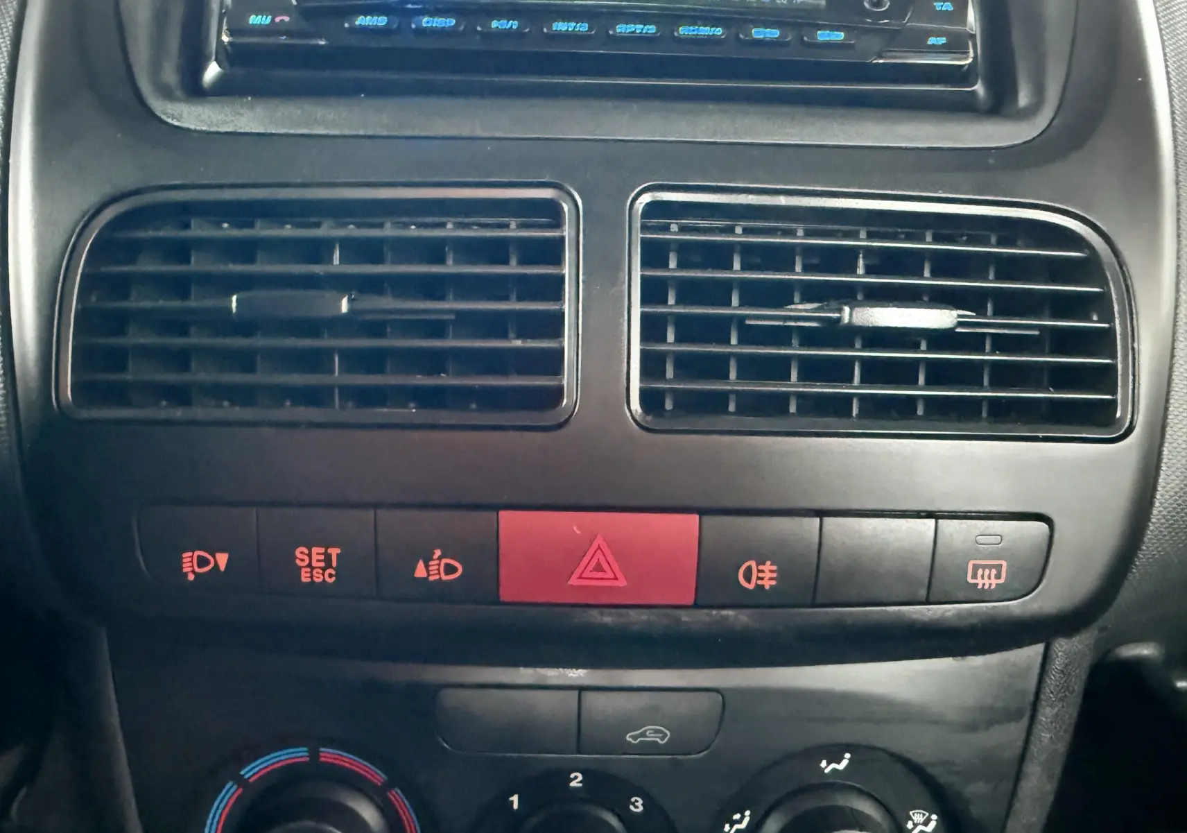 Vue rapprochée du tableau de bord du Fiat Doblo Cargo 2011, montrant les aérateurs et commandes de climatisation noires.