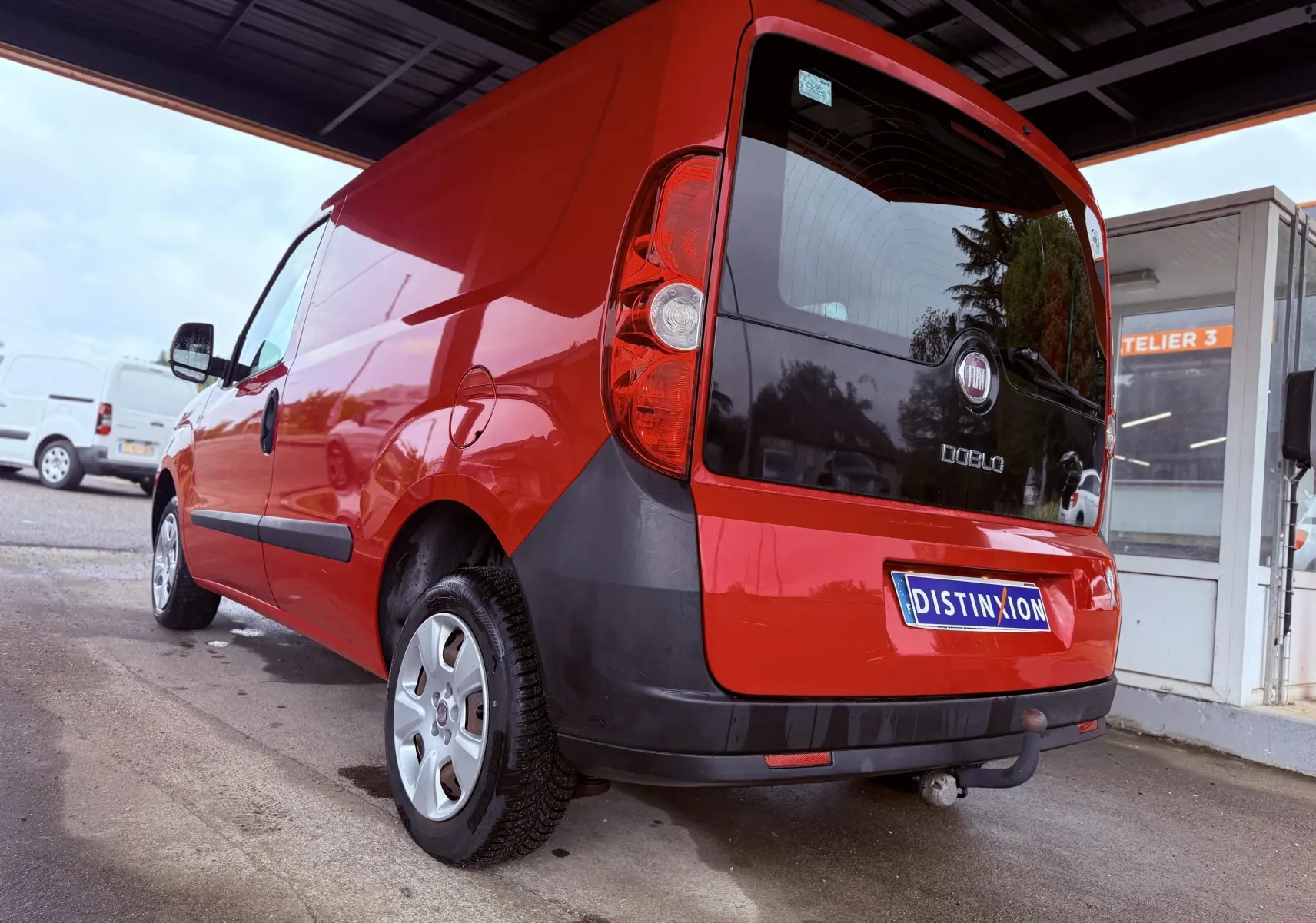 Fiat Doblo Cargo rouge vue 3/4 arrière droit, avec hayon noir et attelage visible sous le pare-chocs.