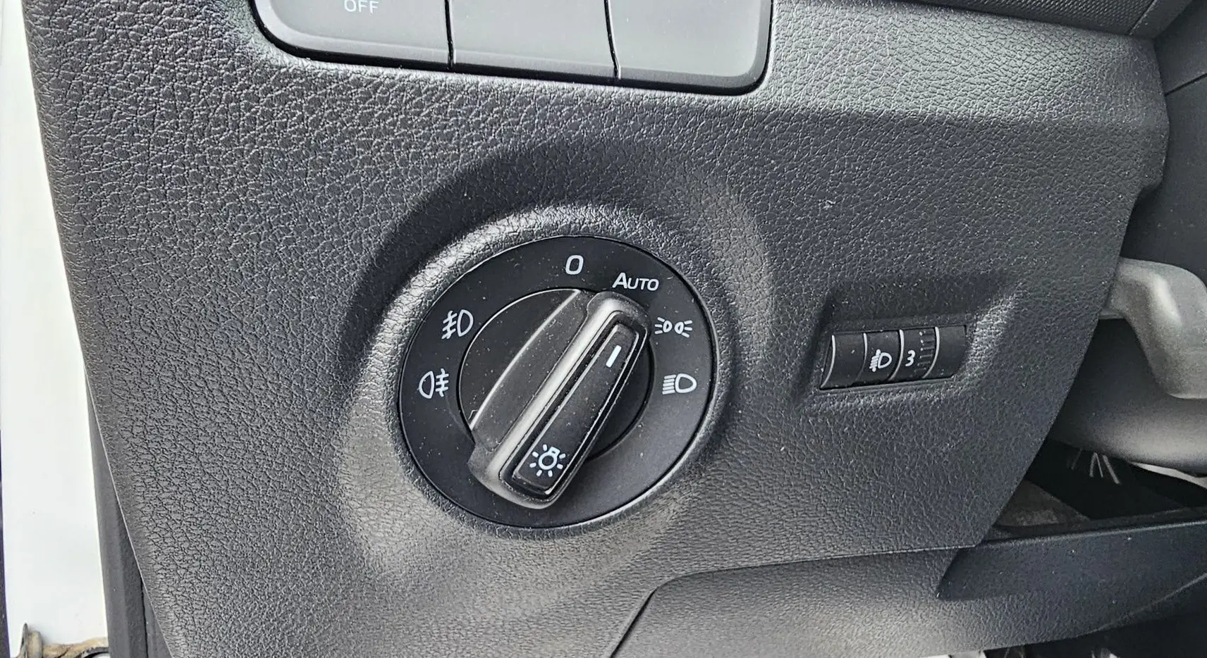 Gros plan sur le bouton de commande des phares dans l'habitacle noir d'une Skoda Fabia blanche côté gauche.
