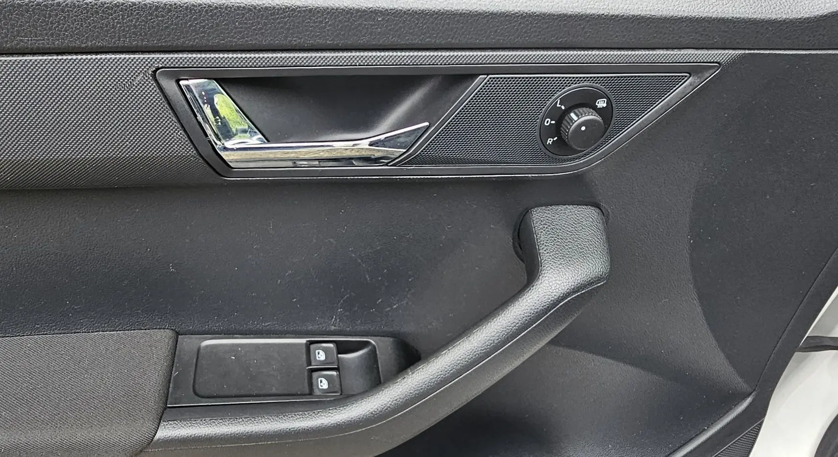 Gros plan sur la porte avant gauche d'une Skoda Fabia blanche, montrant la poignée, les commandes de vitres et le réglage des rétroviseurs.