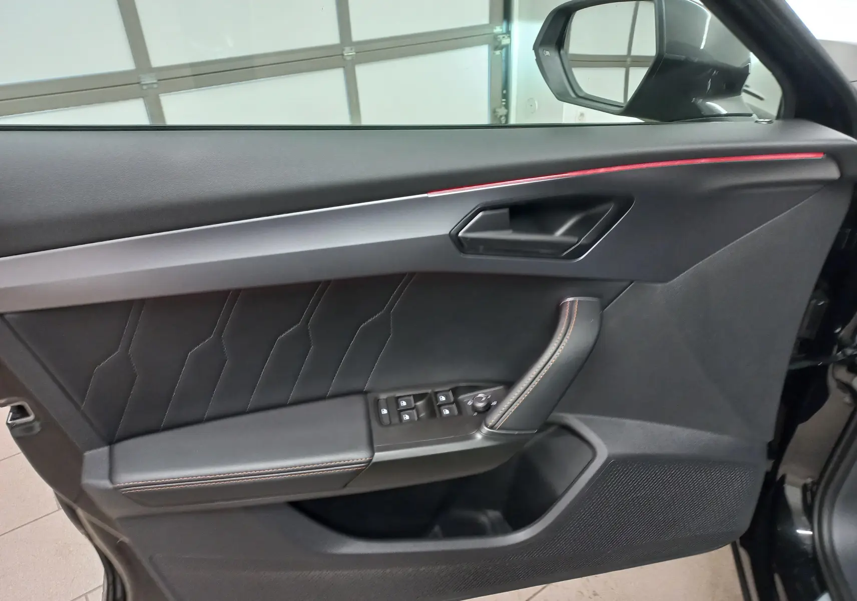 Détail de la porte côté gauche du CUPRA Formentor noir minuit avec surpiqûres orange et bande lumineuse rouge.