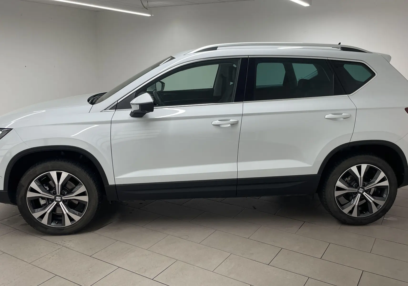 Profil droit du SUV SEAT Ateca blanc Nevada avec jantes alliage 18 pouces et toit équipé de barres de toit.