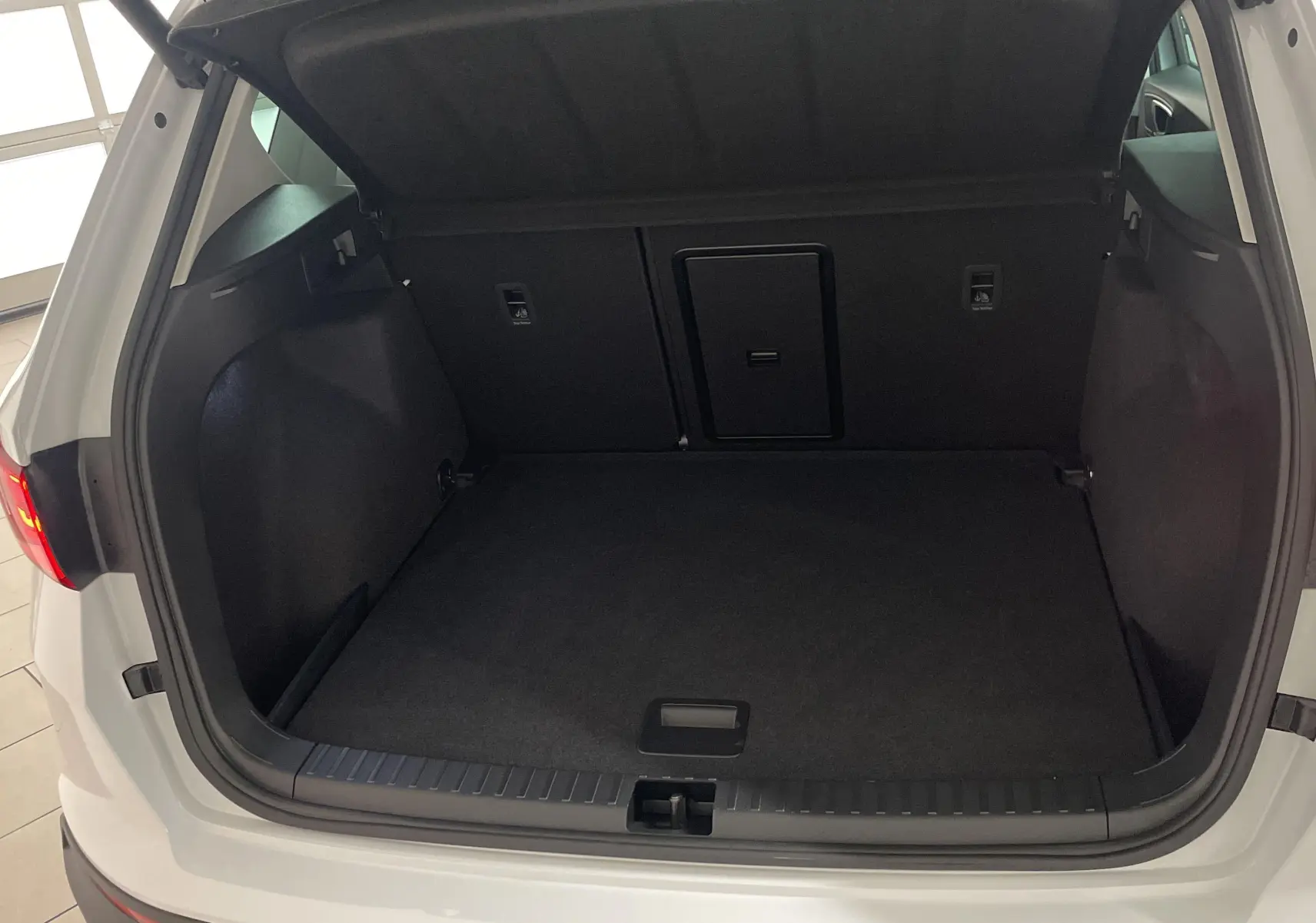 Coffre ouvert en vue arrière d'un SEAT Ateca blanc Nevada avec hayon électrique et feux arrière allumés.