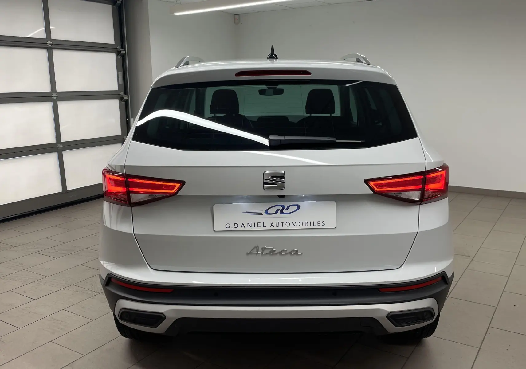 Vue arrière d'un SEAT Ateca blanc Nevada 2024 avec feux allumés et hayon électrique en intérieur showroom.