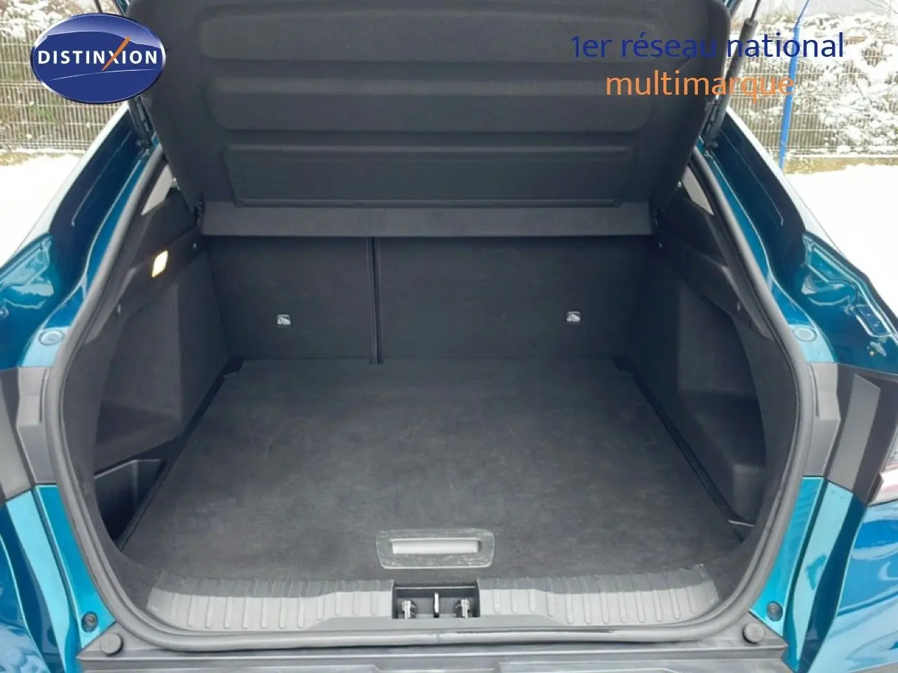 Coffre ouvert vu de l'arrière d'une Renault Arkana bleu Zanzibar métal, montrant l'espace de chargement vide.