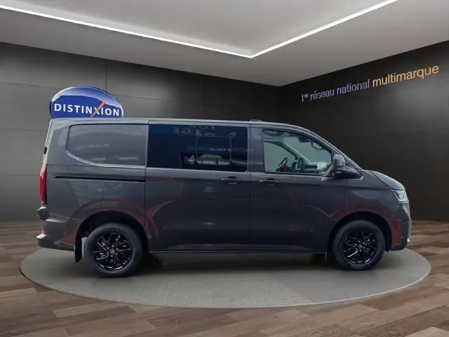 Vue latérale droite d'un Volkswagen Transporter ProCab gris métallisé avec jantes alliage noires brillantes dans un showroom.