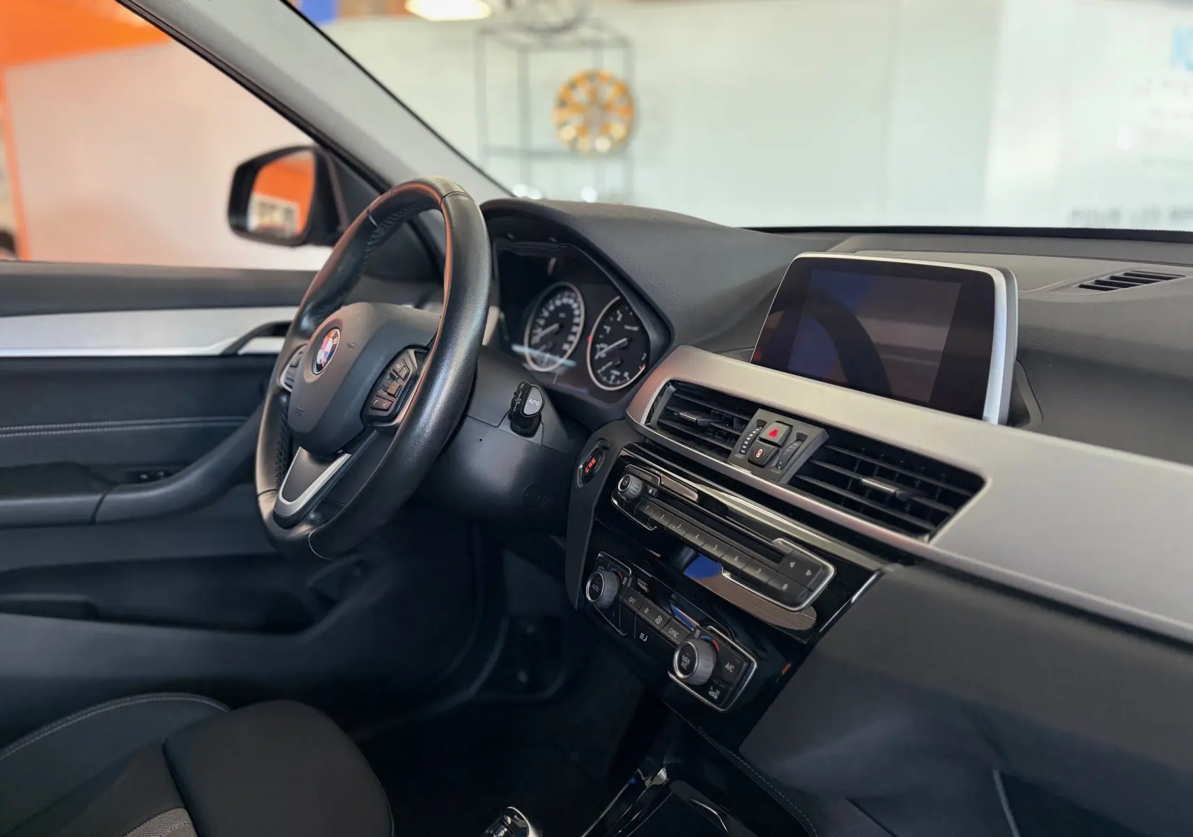 Vue intérieure côté conducteur du tableau de bord noir et écran central de la BMW X1 20i S-DRIVE SPORT LINE 2018.