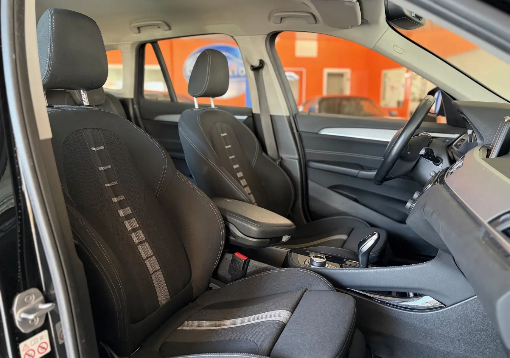 Vue intérieure côté gauche du BMW X1 20i noir de 2018, montrant les sièges avant en tissu noir et la console centrale.