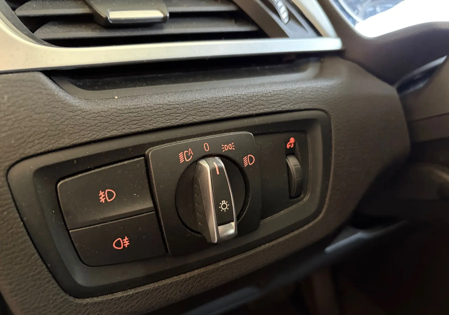Gros plan sur le bouton de commande des phares du tableau de bord noir d'une BMW X1 20i S-DRIVE SPORT LINE 2018.