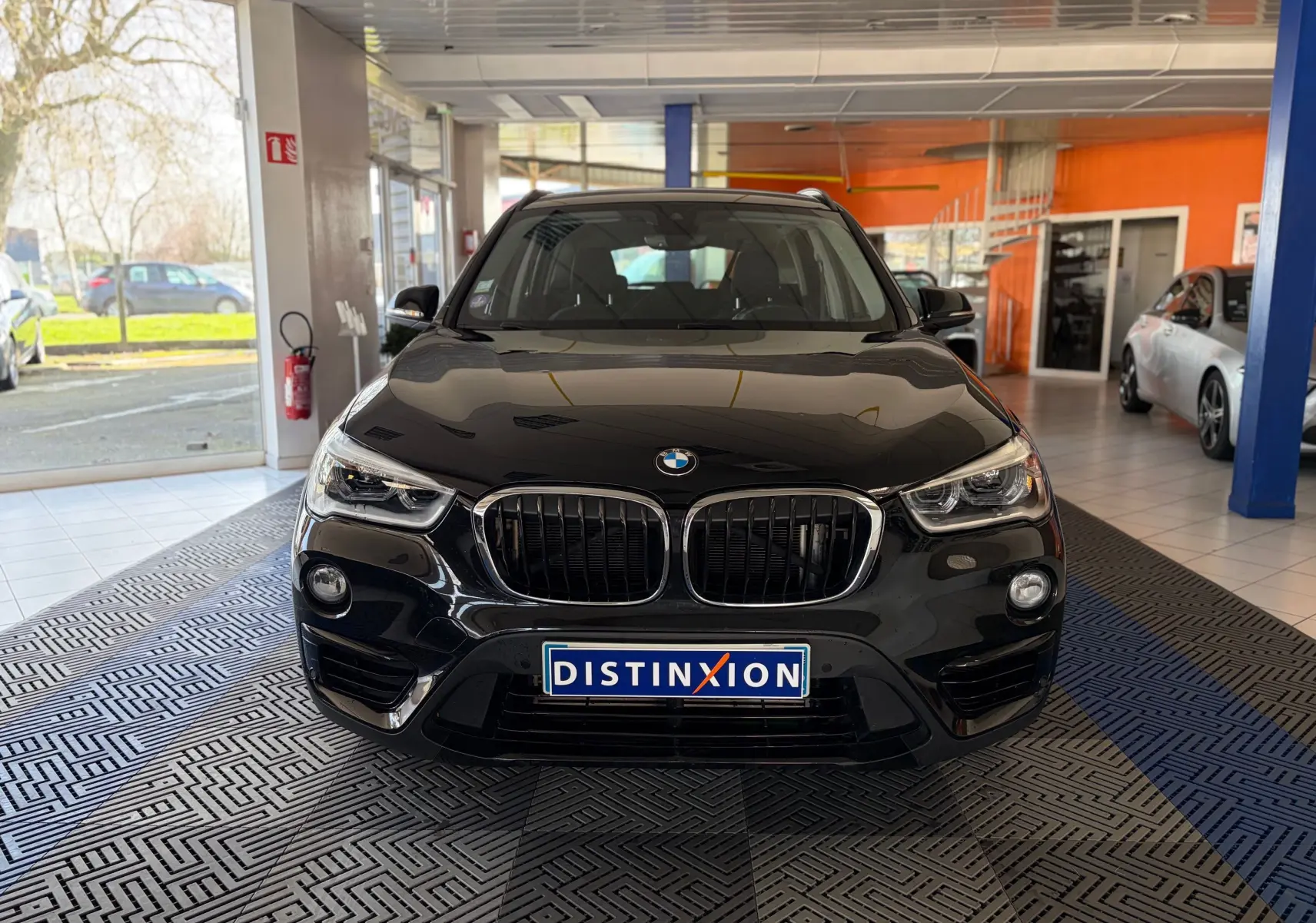 Vue avant d'un BMW X1 noir 2018 en showroom, mettant en valeur sa calandre double haricot et ses phares LED distinctifs.