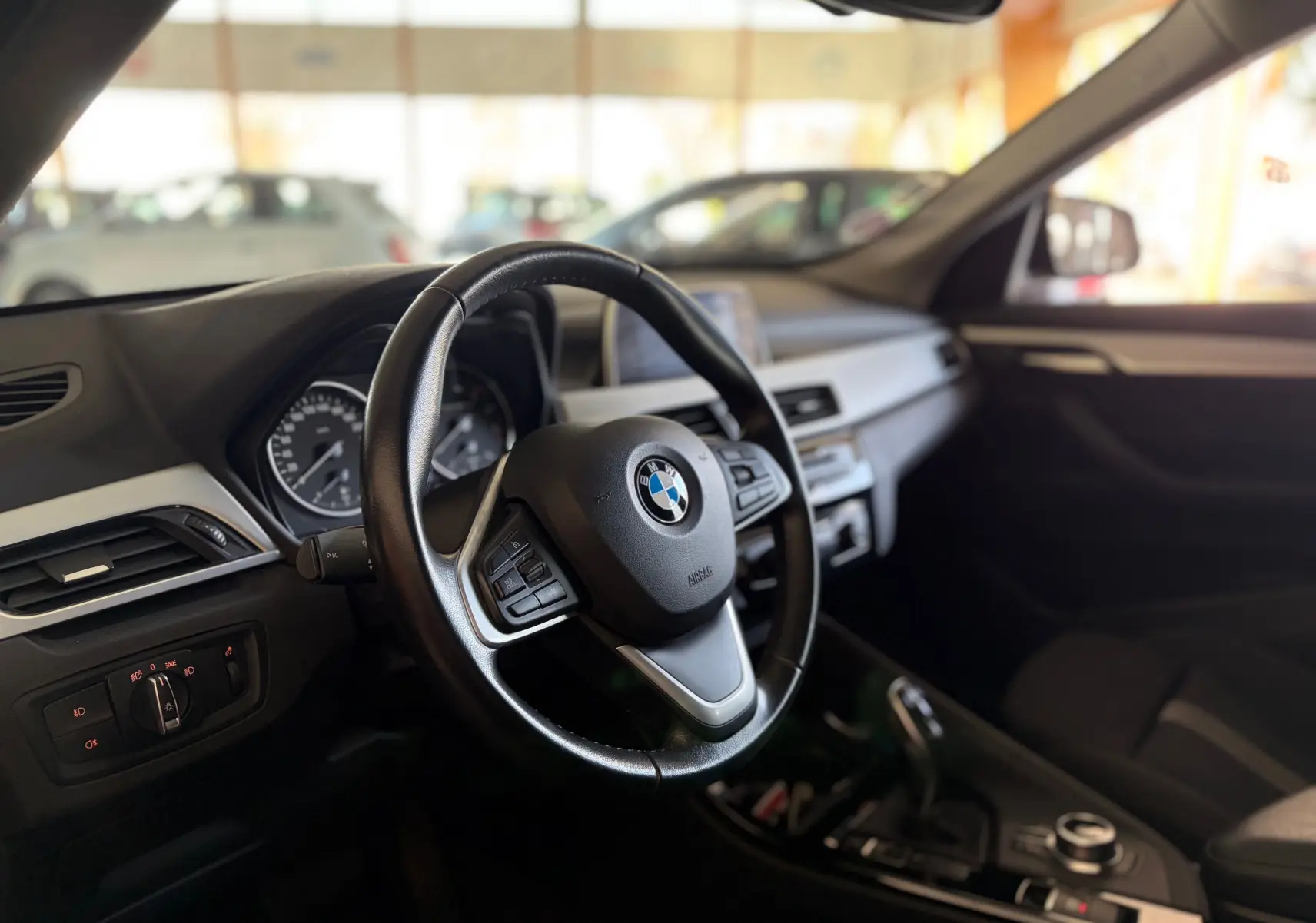 Vue intérieure côté conducteur du BMW X1 noir 2018, mettant en valeur le volant cuir multifonction et le tableau de bord moderne.