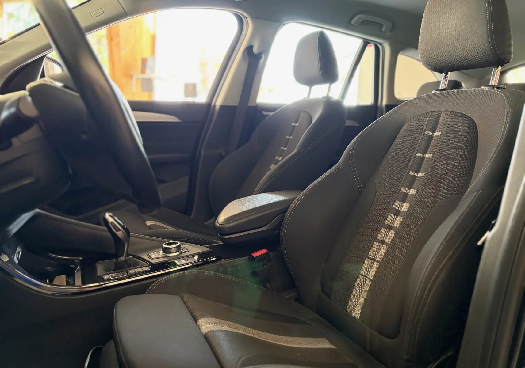 Vue intérieure côté conducteur de la BMW X1 noire 2018, mettant en valeur les sièges tissu noir avec motifs et la console centrale.