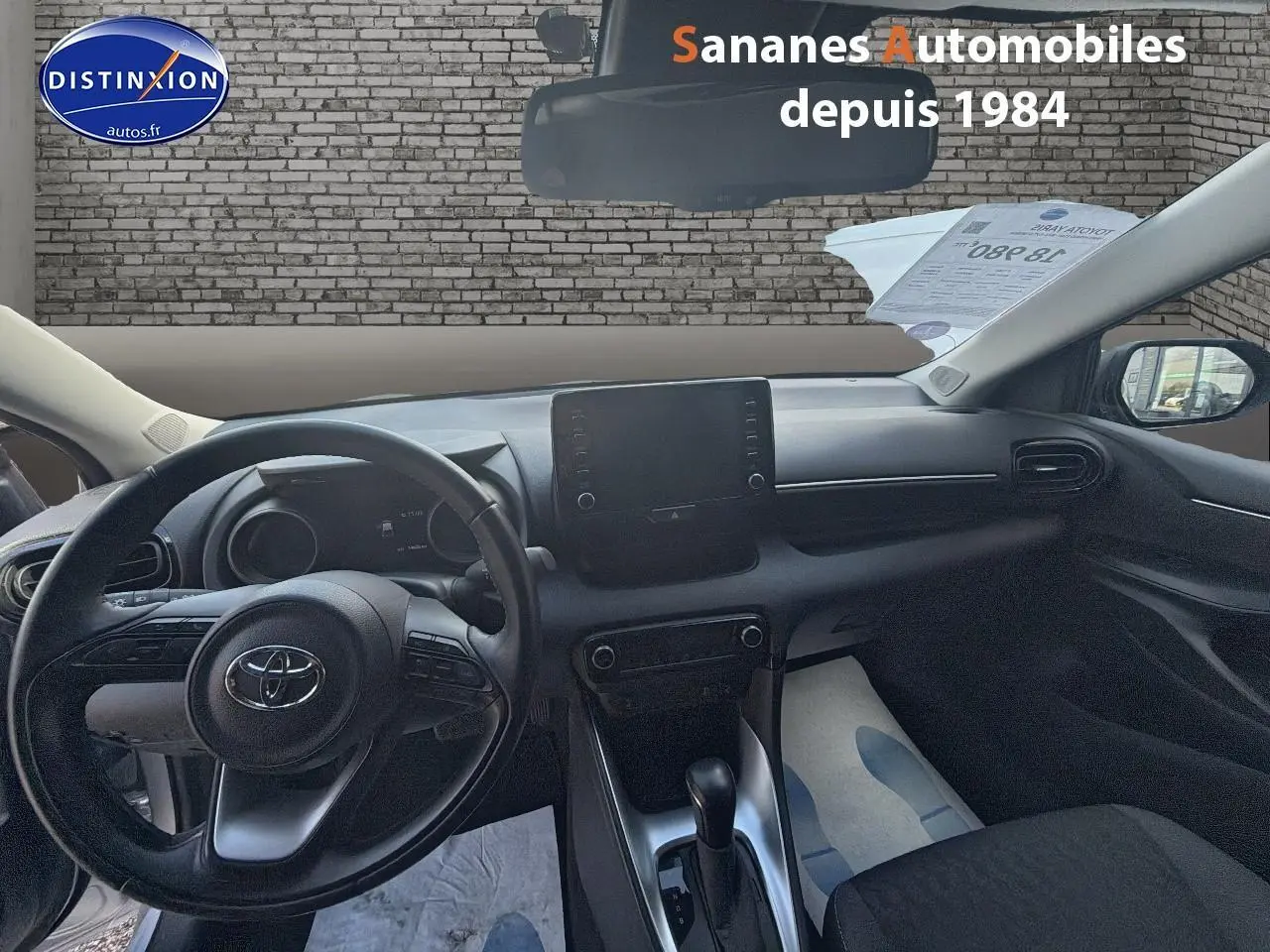 Vue intérieure avant de la Toyota Yaris Hybrid 116h 2023, tableau de bord et volant noirs avec écran tactile central.