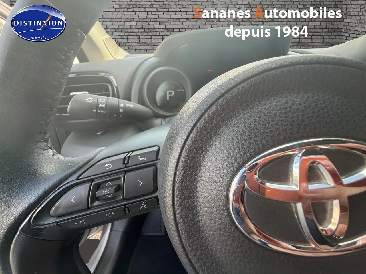 Gros plan sur le volant noir de la Toyota Yaris Hybrid 2023, mettant en valeur les commandes intégrées et le logo chromé.