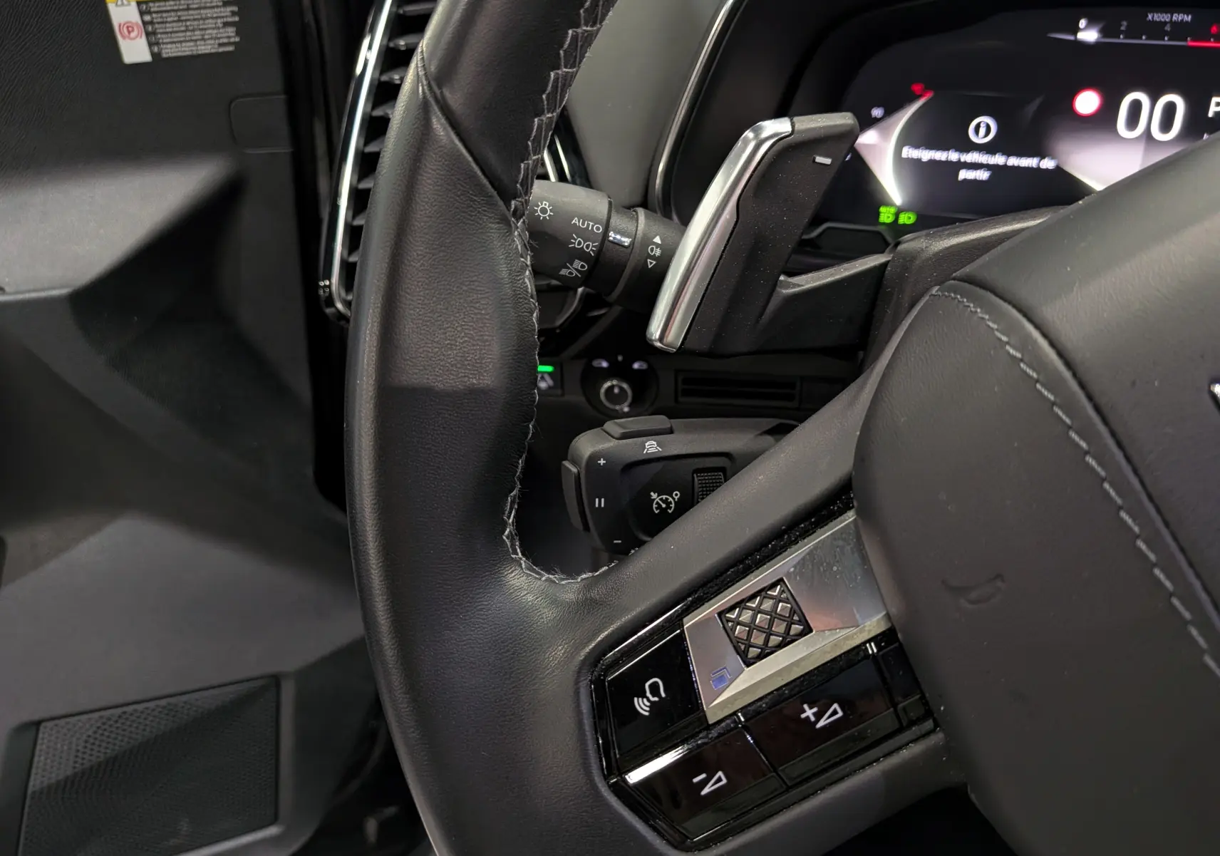 Gros plan sur le volant en cuir noir et les commandes intégrées du DS7 BlueHDi 130 CH EAT8 OPERA 2024, tableau de bord partiel visible.