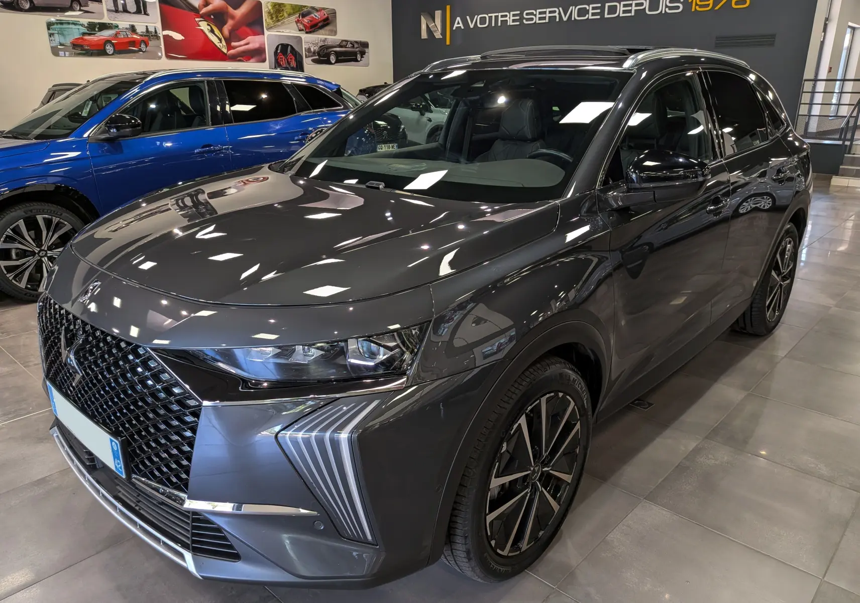 DS7 BlueHDi 130 gris en 3/4 avant droit, avec calandre distinctive et jantes bi-ton en showroom.