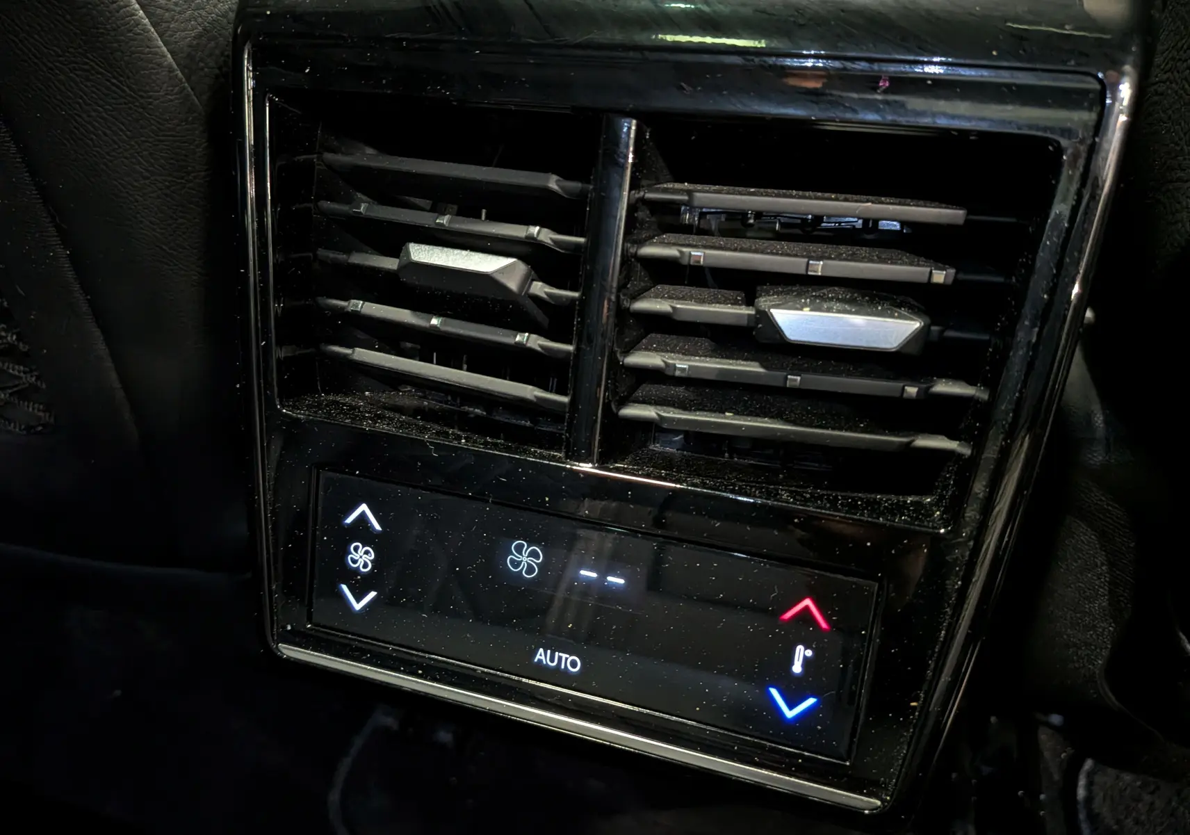 Gros plan sur la commande de climatisation arrière noire du DS7 2024, avec réglages tactiles et aérateurs horizontaux.