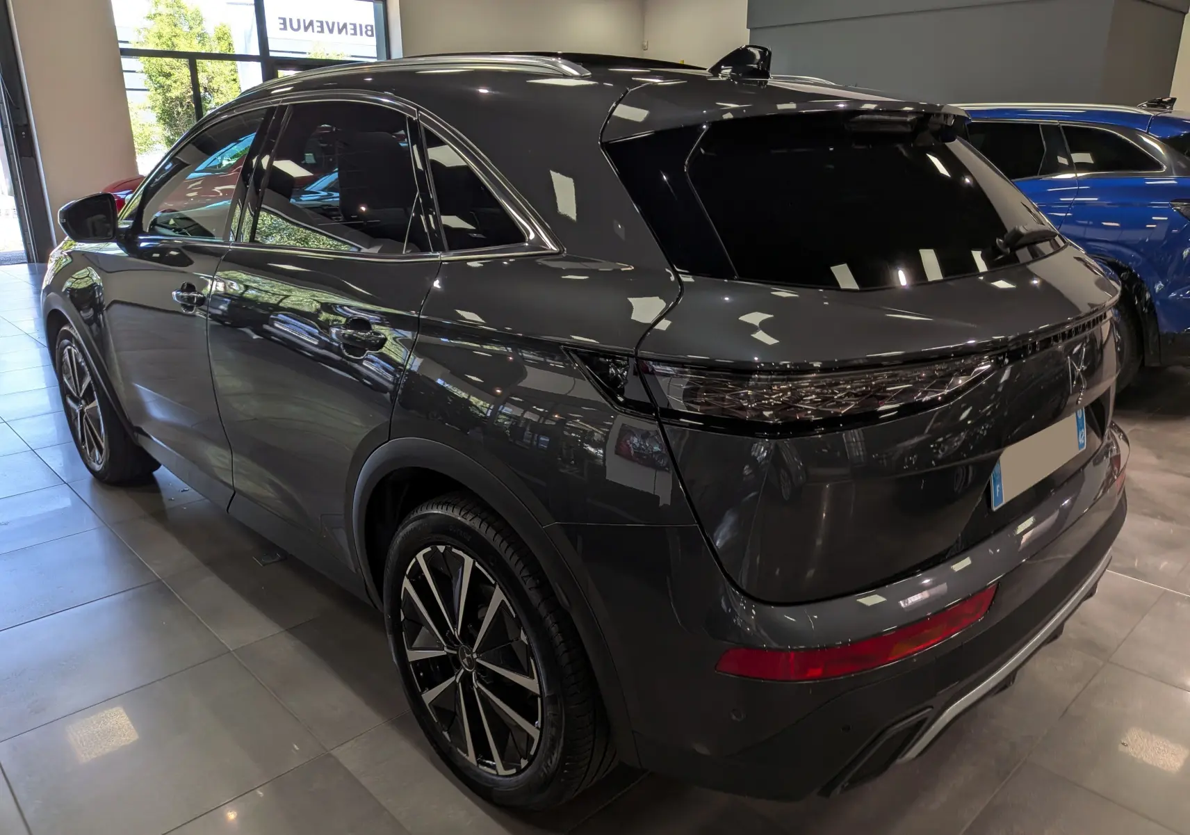 DS7 BlueHDi 130 gris 3/4 arrière droit en showroom, avec jantes bi-ton et feux arrière étirés noirs.