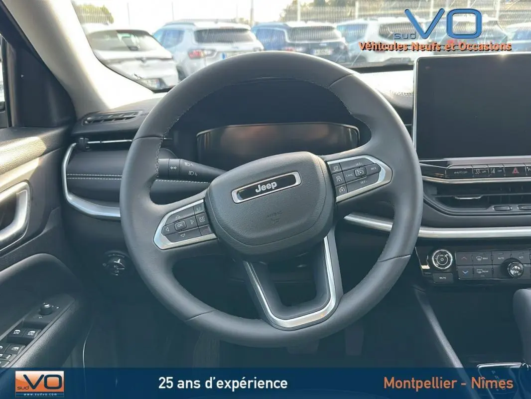 Vue centrée sur le volant noir du Jeep Compass 2024 avec tableau de bord et écran tactile en arrière-plan.