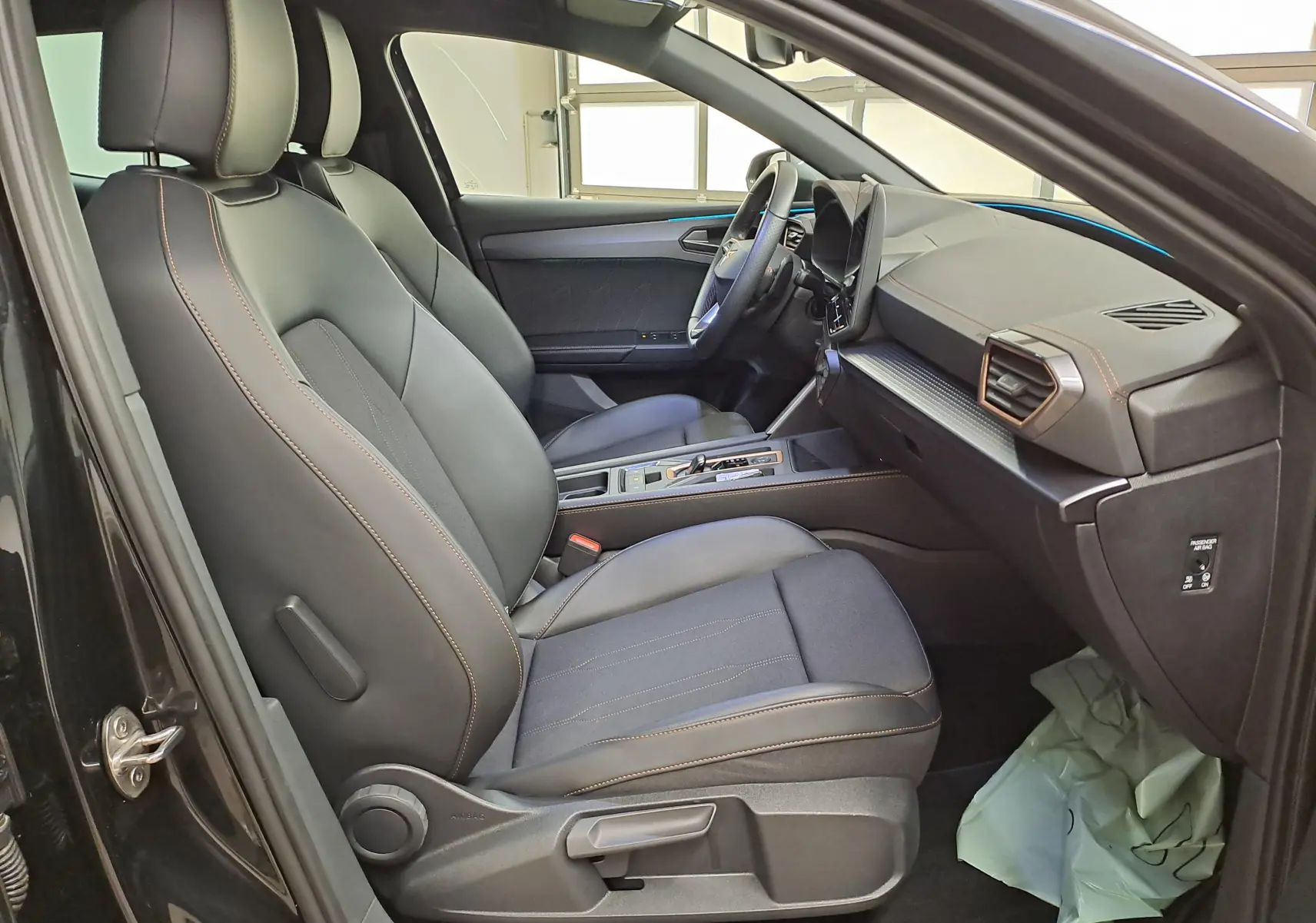 Vue intérieure côté conducteur de la CUPRA Leon Ph.2 1.5 eTSI 150 DSG7 avec sièges noirs et surpiqûres cuivrées.