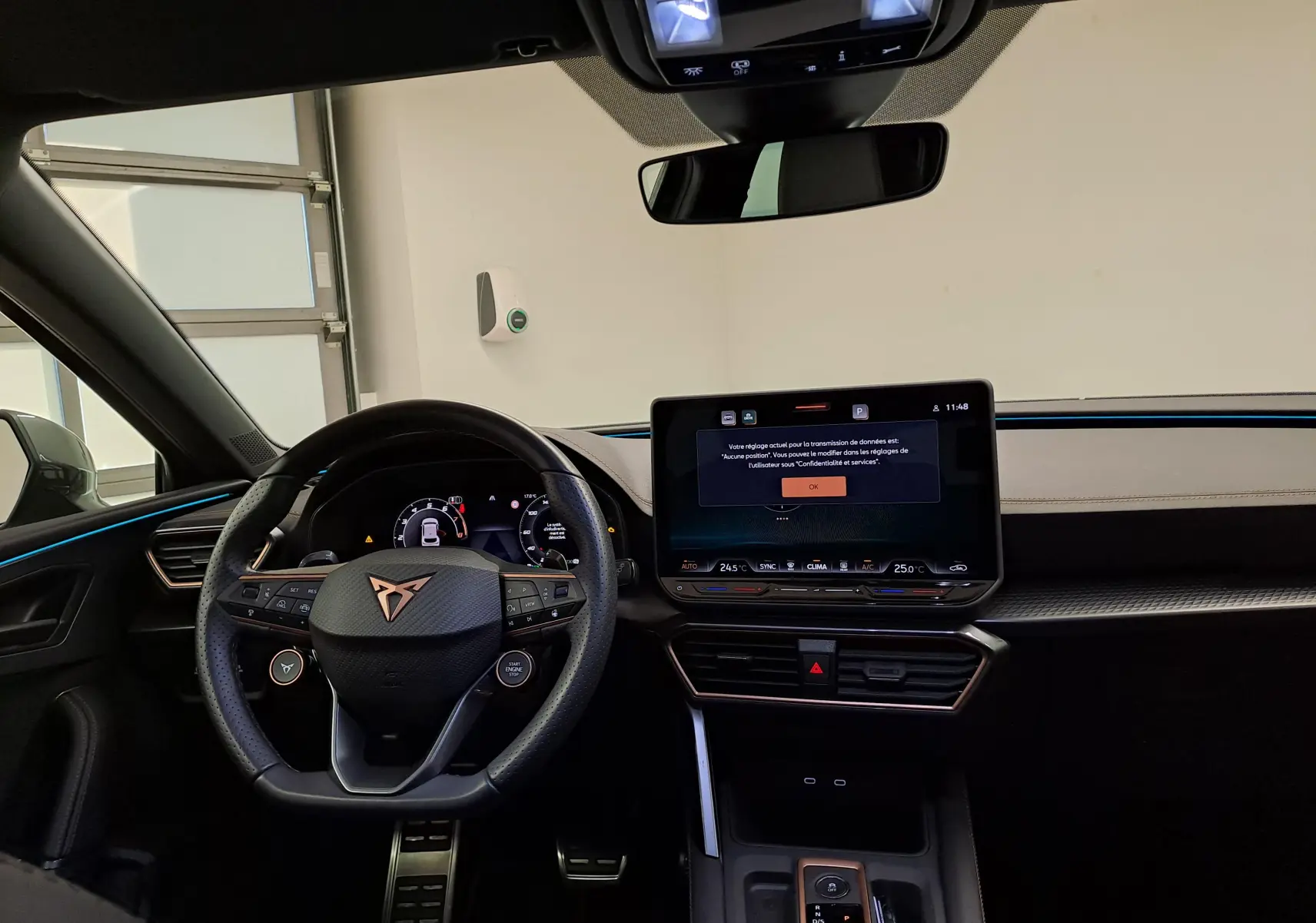 Intérieur de la CUPRA Leon Ph.2 2025, vue du poste de conduite avec volant noir et écran tactile central allumé.