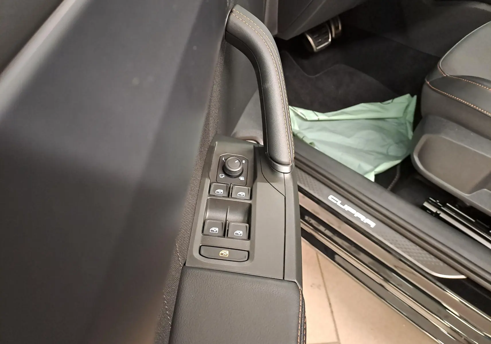 Vue rapprochée de la portière côté gauche d'une CUPRA Leon 2025 noir minuit avec commandes de vitres et seuil de porte lumineux.